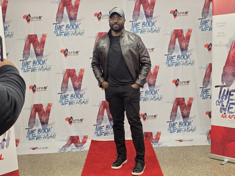 A man in a leather jacket on the red carpet in front of the Book of Nehemiah step-and-repeat backdrop